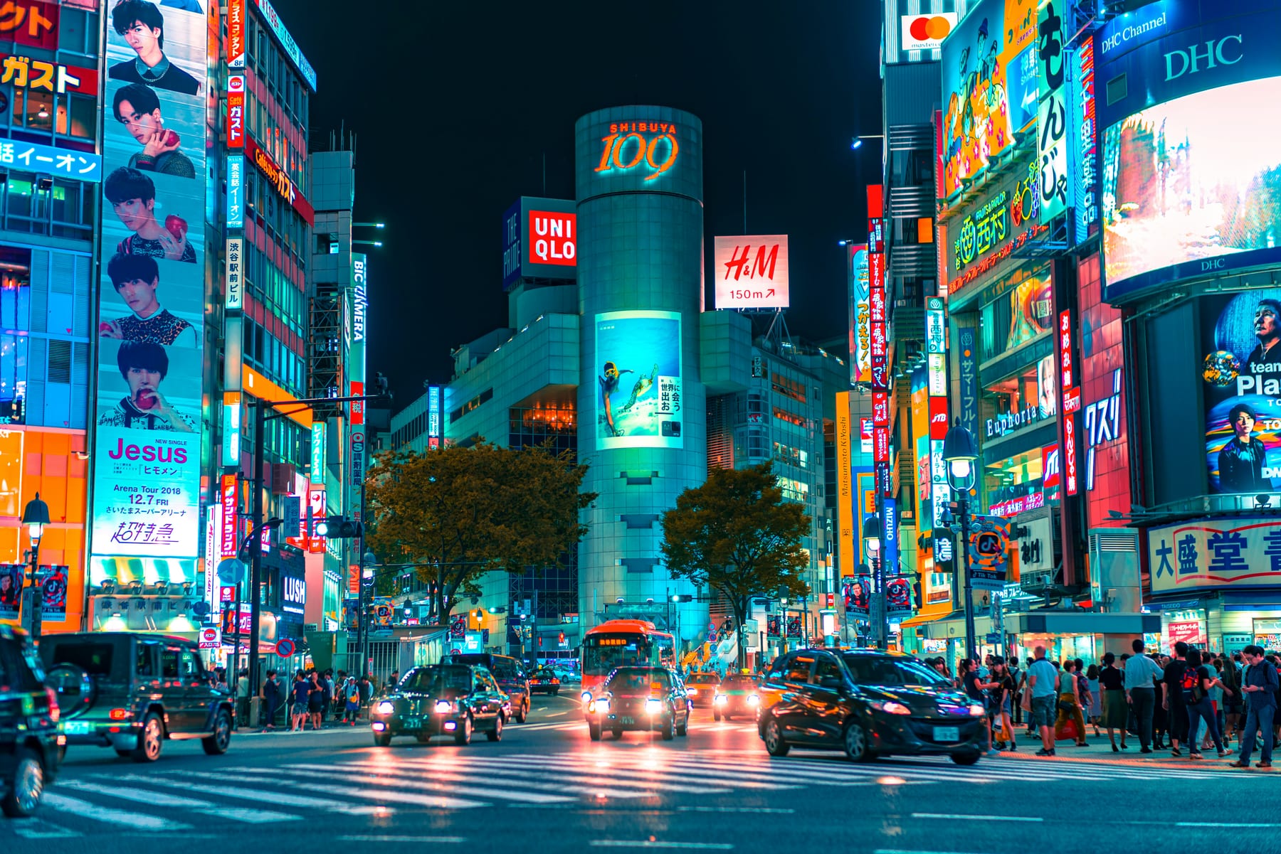 Shibuya Crossing at night — streams of pedestrians crossing under giant illuminated screens
