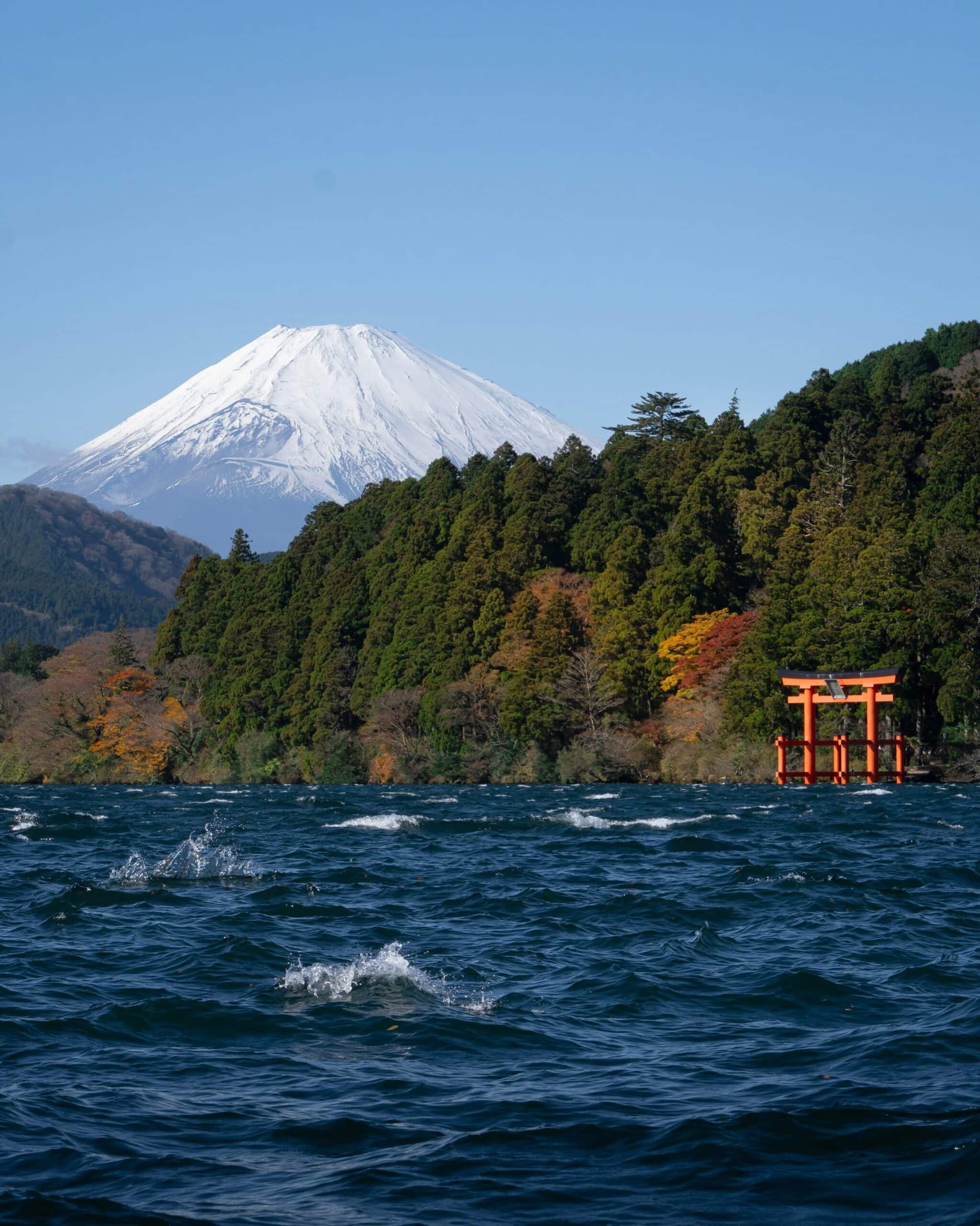 Mount Fuji rising above Lake Ashi in Hakone, the red torii gate of Hakone Shrine at the water's edge, autumn forest, viewed from the lake