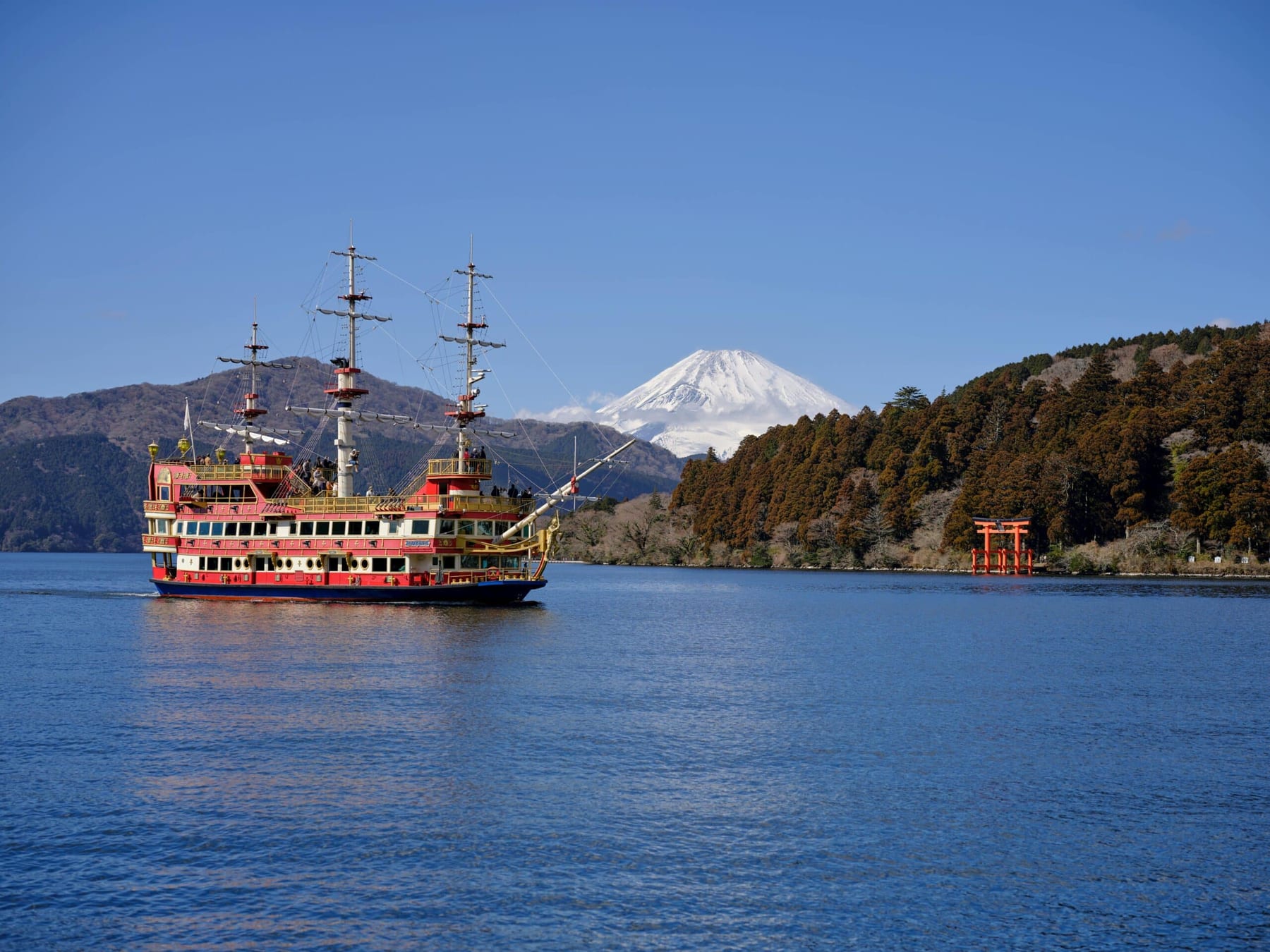 The Lake Ashi pirate cruise ship with Mount Fuji and the Hakone Shrine torii gate visible behind it, clear winter sky