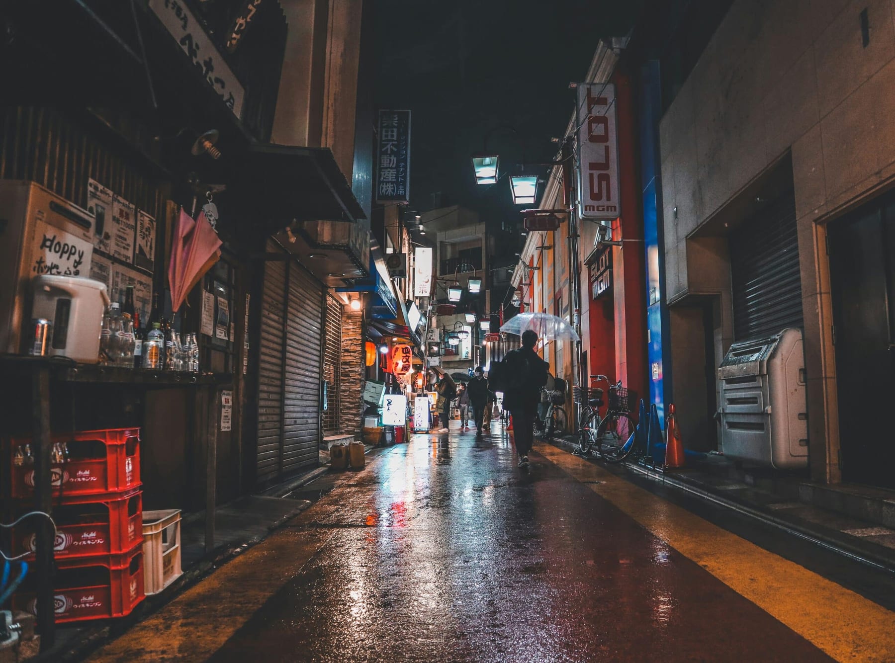 A narrow Japanese backstreet at night in the rain, wet cobblestones reflecting the orange glow of izakaya signs and hanging lanterns