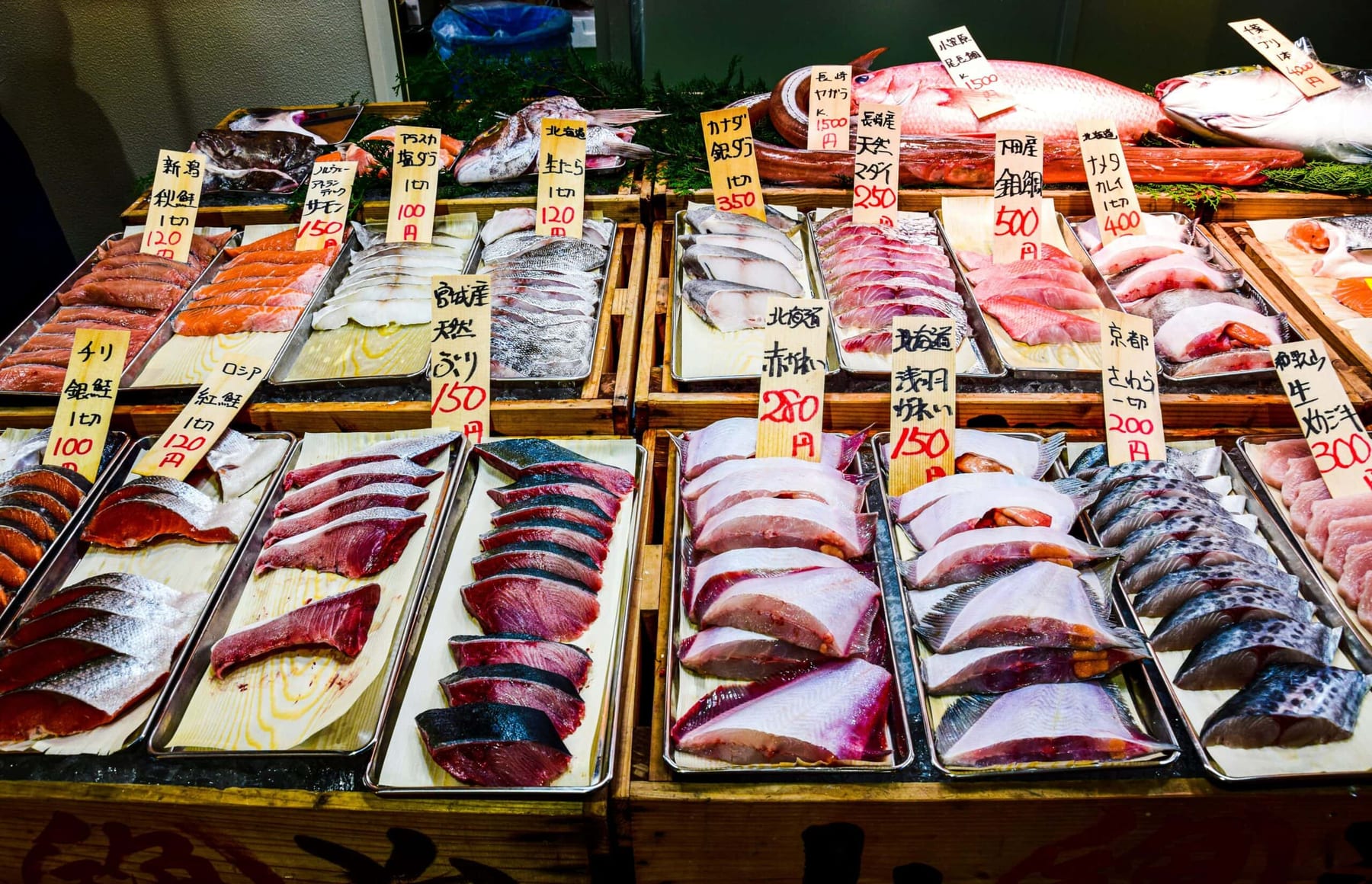 Trays of fresh fish and seafood displayed at a Japanese market with handwritten price tags in yen