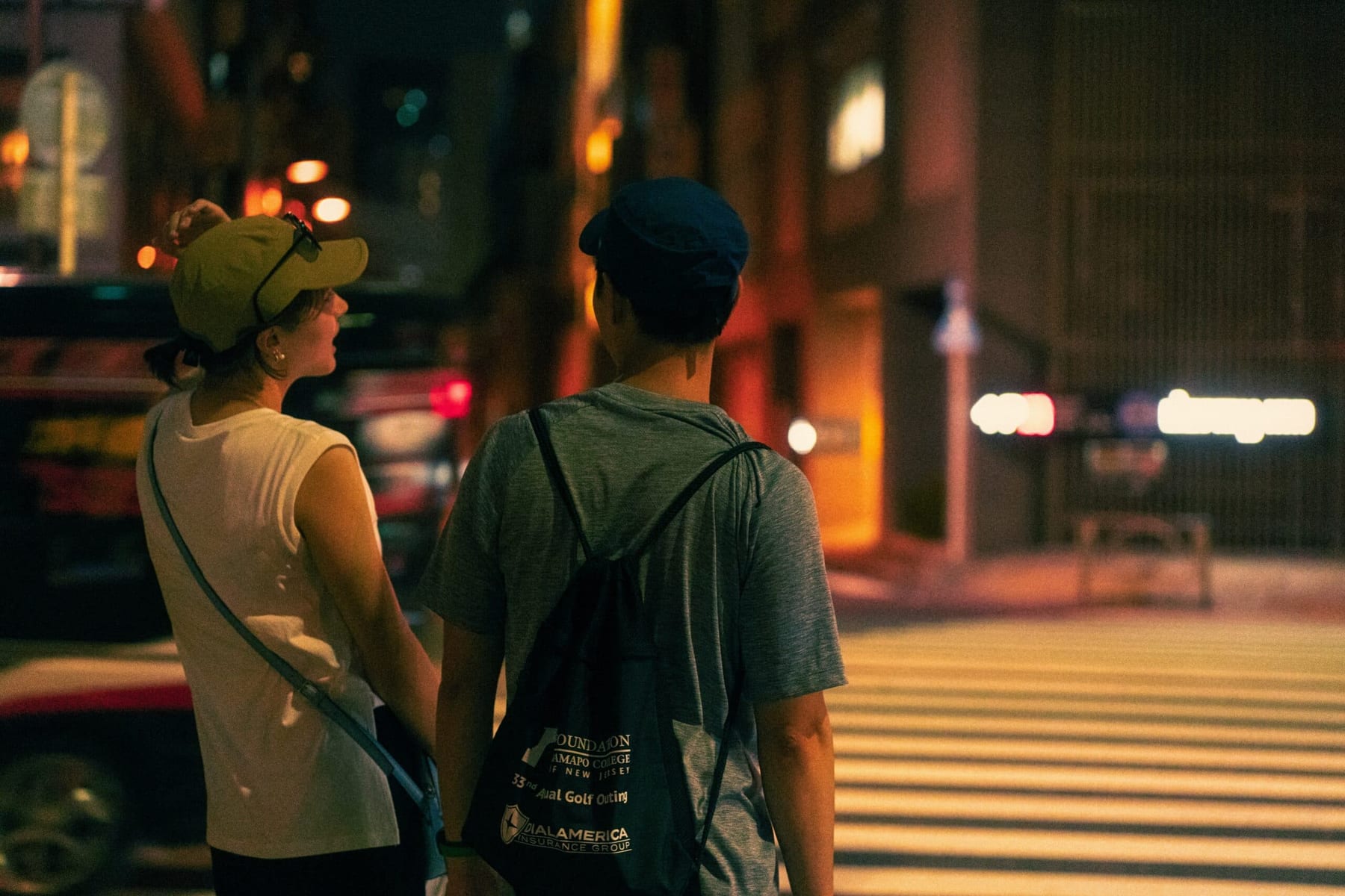 Two people in light summer clothing, a sleeveless top and cap, seen from behind on a Tokyo street at night
