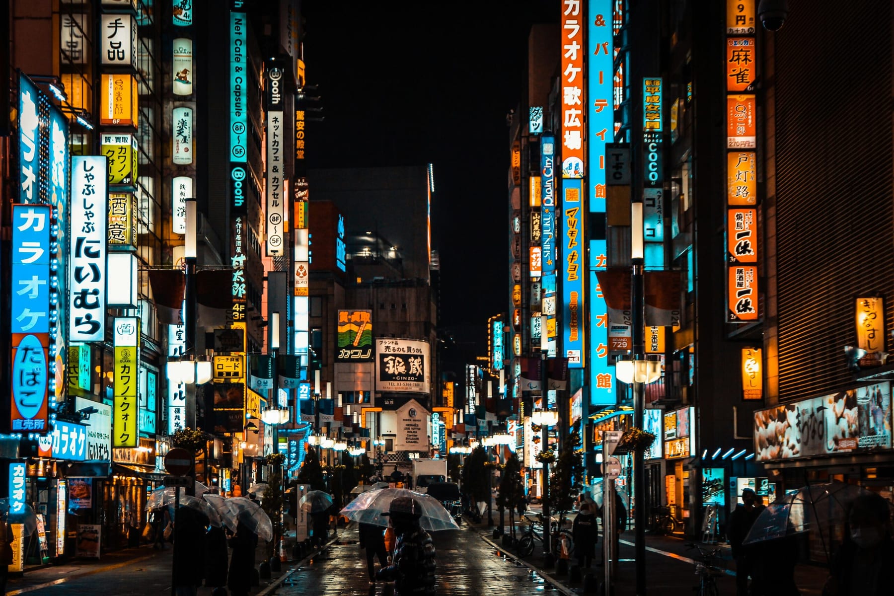 Pedestrians with transparent umbrellas walking through the neon-lit streets of Shinjuku at night during the rainy season