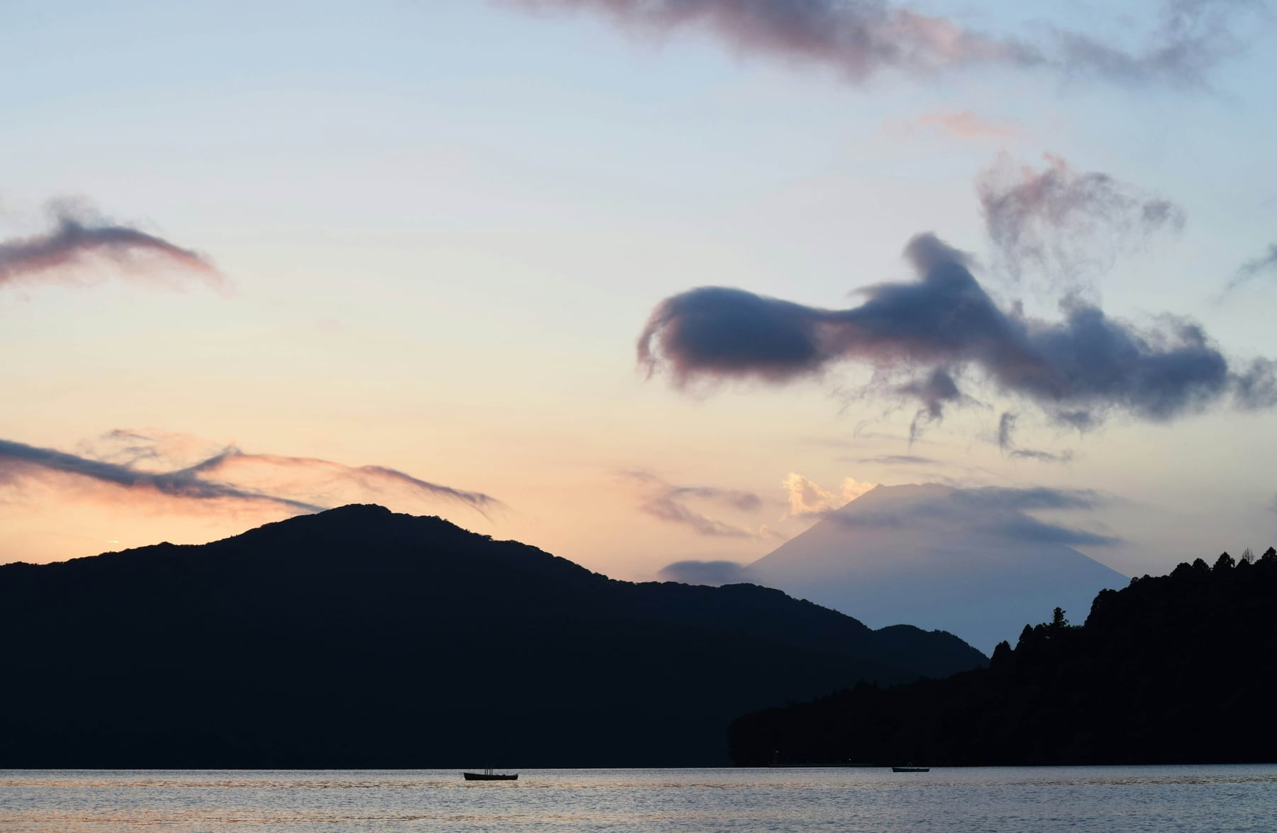 Mount Fuji at sunset seen from Lake Ashi in Hakone with soft pink clouds and silhouetted mountain ridgeline