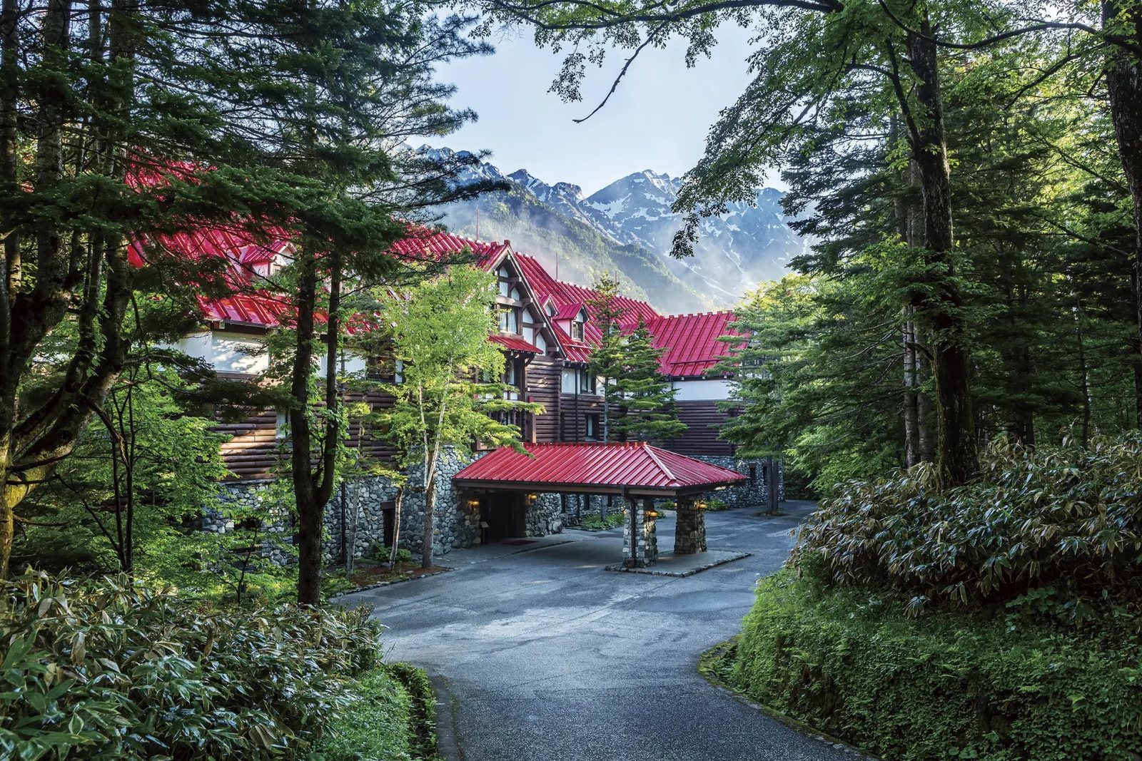 The red-roofed Kamikochi Imperial Hotel among the trees, with the Alps behind