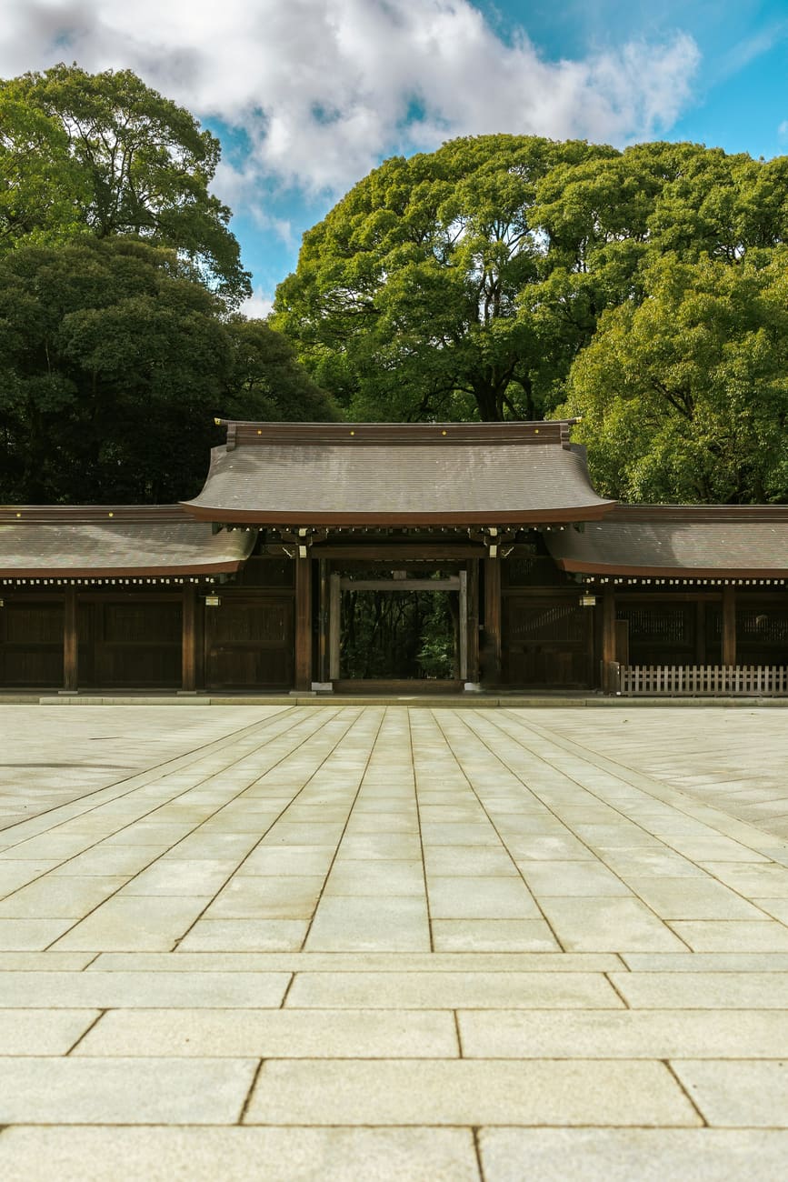 A plain cypress shrine building behind a gravel court